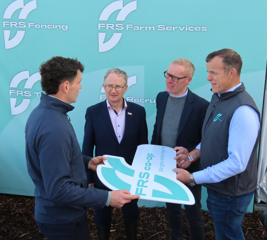 Four men stand smiling at an FRS Co-op event, holding a large FRS Co-op sign with the slogan ‘We grow better together.’ FRS Fencing and FRS Farm Services branding is displayed in the background.