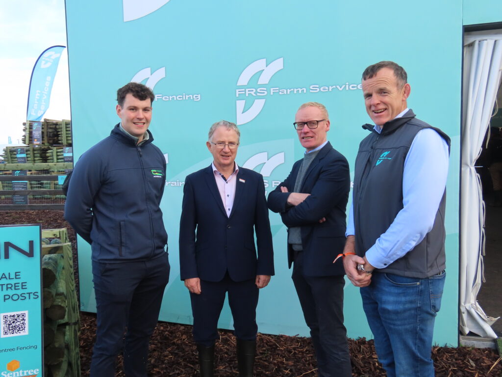 Four men stand together at an FRS Co-op event in front of an FRS Farm Services backdrop, smiling for the camera.